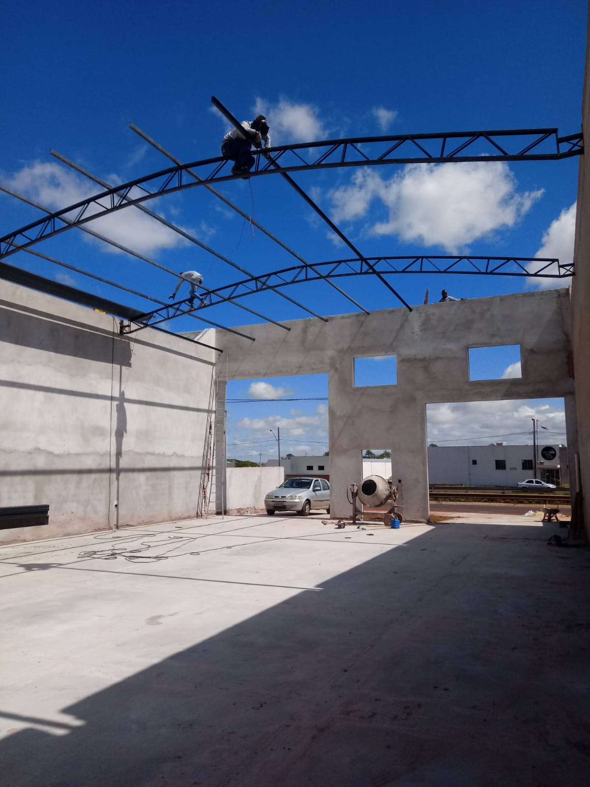 Soldador montando tesoura metálica em arco sobre galpão